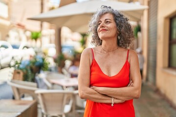 Middle age grey-haired woman smiling confident standing with arms crossed gesture at street