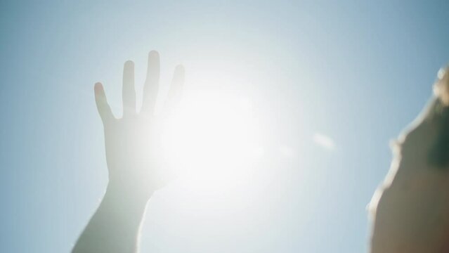 Man closing sun by hand, blue sky, covering sunlight with arm. Young person looking at bright light.