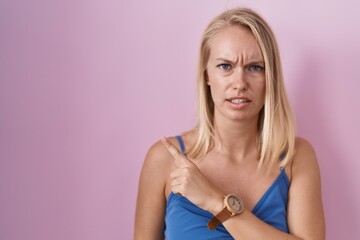 Young caucasian woman standing over pink background pointing aside worried and nervous with...