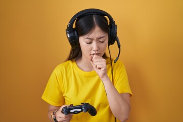 Chinese young woman playing video game holding controller feeling unwell and coughing as symptom for cold or bronchitis. health care concept.