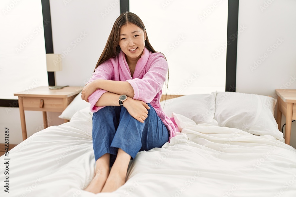 Poster young chinese girl smiling happy sitting on the bed at bedroom.