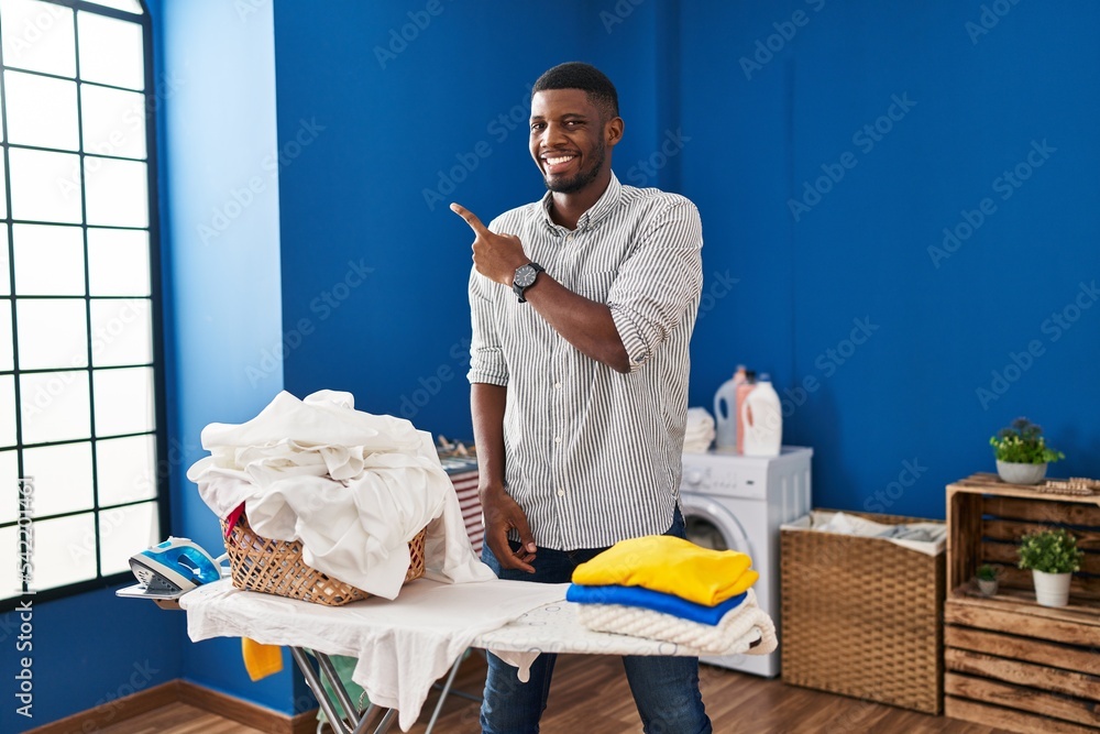 Poster african american man ironing clothes at home smiling cheerful pointing with hand and finger up to th