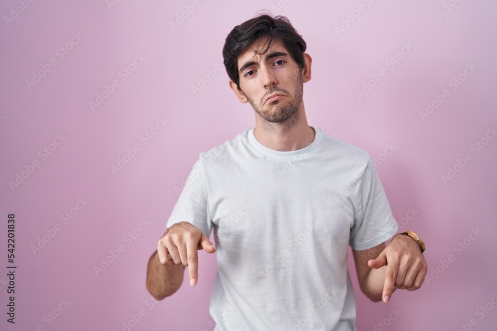 Canvas Prints Young hispanic man standing over pink background pointing down looking sad and upset, indicating direction with fingers, unhappy and depressed.