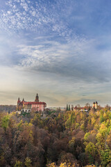 A photo of Książ Castle in Wałbrzych set against a beautiful autumn sky. The castle, with its impressive architecture, stands out against the picturesque background of the colorful fall foliage