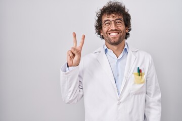 Hispanic young man wearing doctor uniform showing and pointing up with fingers number two while smiling confident and happy.