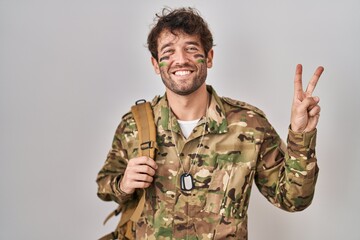 Hispanic young man wearing camouflage army uniform smiling with happy face winking at the camera...
