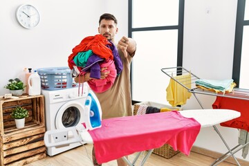 Young handsome man holding laundry ready to iron with angry face, negative sign showing dislike...