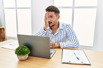 Young handsome man with beard working at the office using computer laptop covering one eye with...