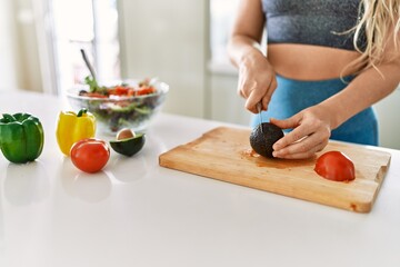 Young woman cutting avocado for salad at kitchen