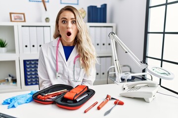 Young beautiful doctor woman with reflex hammer and medical instruments afraid and shocked with surprise expression, fear and excited face.