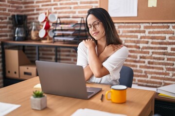 Hispanic young woman working at the office wearing glasses hugging oneself happy and positive, smiling confident. self love and self care