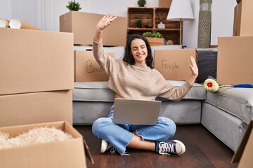 Young hispanic woman using laptop sitting on floor at new home