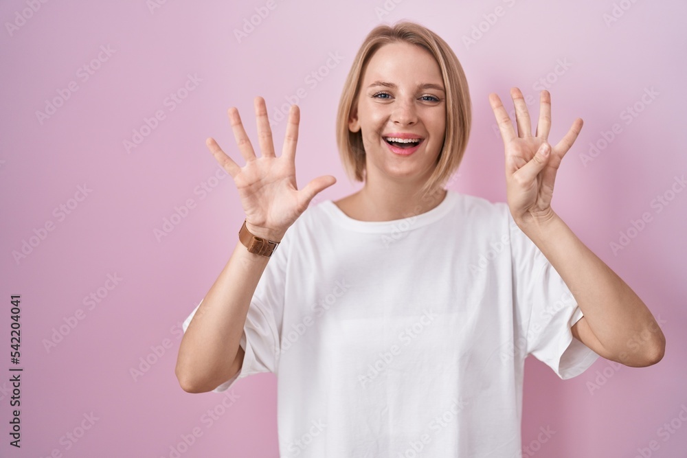 Sticker young caucasian woman standing over pink background showing and pointing up with fingers number nine