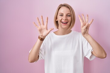 Young caucasian woman standing over pink background showing and pointing up with fingers number...