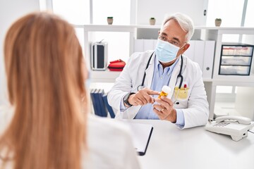Middle age man and woman doctor and patient wearing medical mask holding pills at clinic