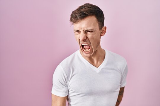 Caucasian man standing over pink background angry and mad screaming frustrated and furious, shouting with anger. rage and aggressive concept.