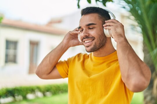 Young hispanic man listening to music standing at park