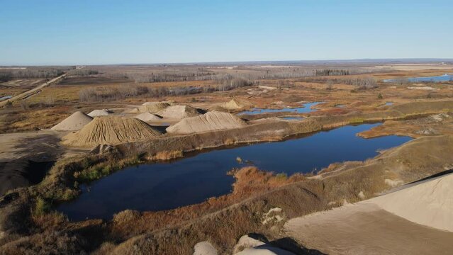 Drone moving forward above a gravel pit with different colored pile and pits full of water. Taken in the late fall with brown colors
