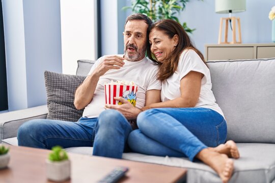 Middle age man and woman couple watching movie sitting on sofa at home