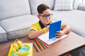 Adorable hispanic boy using touchpad sitting on floor at home