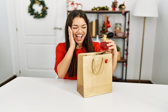 Young latin woman holding perfume of gift bag sitting by christmas decor at home