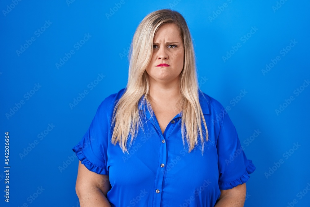 Sticker caucasian plus size woman standing over blue background skeptic and nervous, frowning upset because 