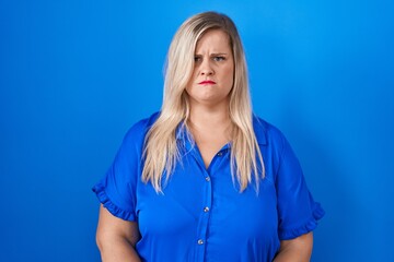 Caucasian plus size woman standing over blue background skeptic and nervous, frowning upset because of problem. negative person.