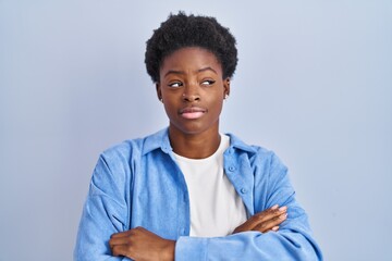 African american woman standing over blue background looking to the side with arms crossed convinced and confident