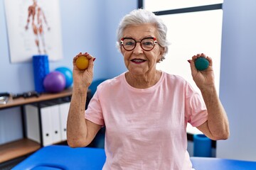 Senior woman with grey hair holding hands strength balls smiling with a happy and cool smile on face. showing teeth.