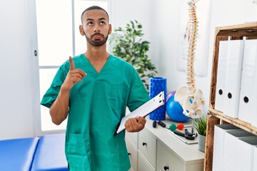 African american physiotherapist man working at pain recovery clinic pointing up looking sad and upset, indicating direction with fingers, unhappy and depressed.