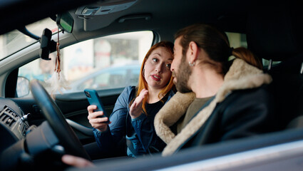 Man and woman couple using smartphone driving car at street