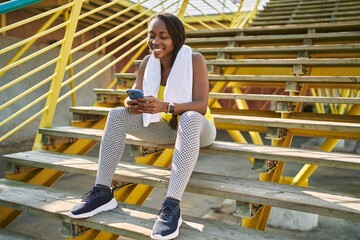 Fototapeta na wymiar African american woman using smartphone sitting on stairs at street