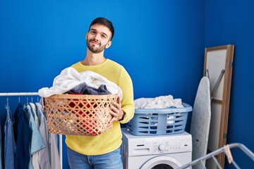 Hispanic man holding laundry basket relaxed with serious expression on face. simple and natural...
