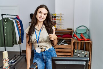 Young brunette woman working as manager at retail boutique smiling happy and positive, thumb up doing excellent and approval sign