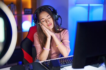 Young hispanic woman playing video games sleeping tired dreaming and posing with hands together while smiling with closed eyes.