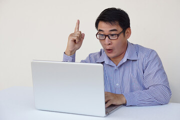 Handsome Asian man office worker feels surprised and got the idea during surfing internet on laptop computer. Point finger up. Concept : work online. Daily Life digital, technology smart device. 