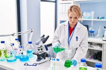 Fototapeta premium Young blonde woman scientist pouring liquid on test tube at laboratory