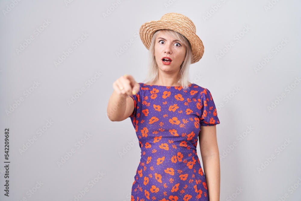 Poster Young caucasian woman wearing flowers dress and summer hat pointing displeased and frustrated to the camera, angry and furious with you