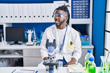 African man with dreadlocks working at scientist laboratory looking to side, relax profile pose with natural face and confident smile.