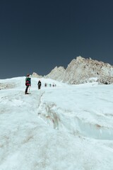 Hikers in the mountain range and rocky landscape covered with snow and ice, vertical
