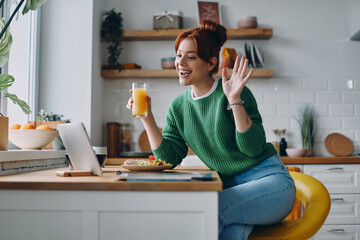 Beautiful young woman having video call while dinning at the domestic kitchen