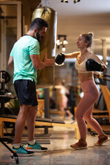 Fit girl with boxing gloves hitting a punching bag. Male fitness instructor with a female client...