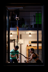 Obraz na płótnie Canvas Fit girl with exercising with ropes with a male fitness instructor in a fitness studio. View from outside the window.