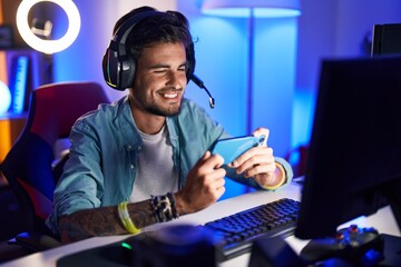 Young hispanic man with tattoos playing video games with smartphone looking positive and happy standing and smiling with a confident smile showing teeth © Krakenimages.com