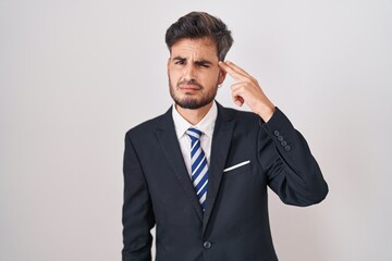 Young hispanic man with tattoos wearing business suit and tie shooting and killing oneself pointing hand and fingers to head like gun, suicide gesture.