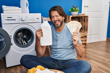 Handsome middle age man saving money of laundry detergent winking looking at the camera with sexy expression, cheerful and happy face.