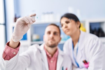 Man and woman wearing scientists uniform looking sample at laboratory