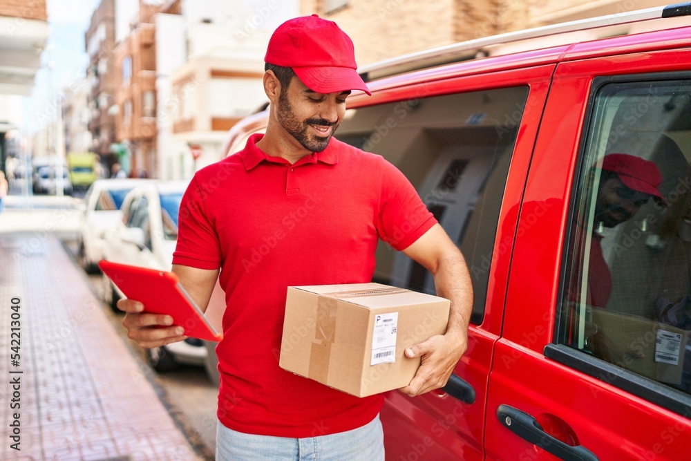 Canvas Prints Young hispanic man courier using touchpad holding package at street