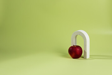 An empty stage with one white concrete arch under it a red apple. On a green background and a shadow from sunlight