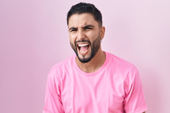 Hispanic young man standing over pink background angry and mad screaming frustrated and furious, shouting with anger. rage and aggressive concept.